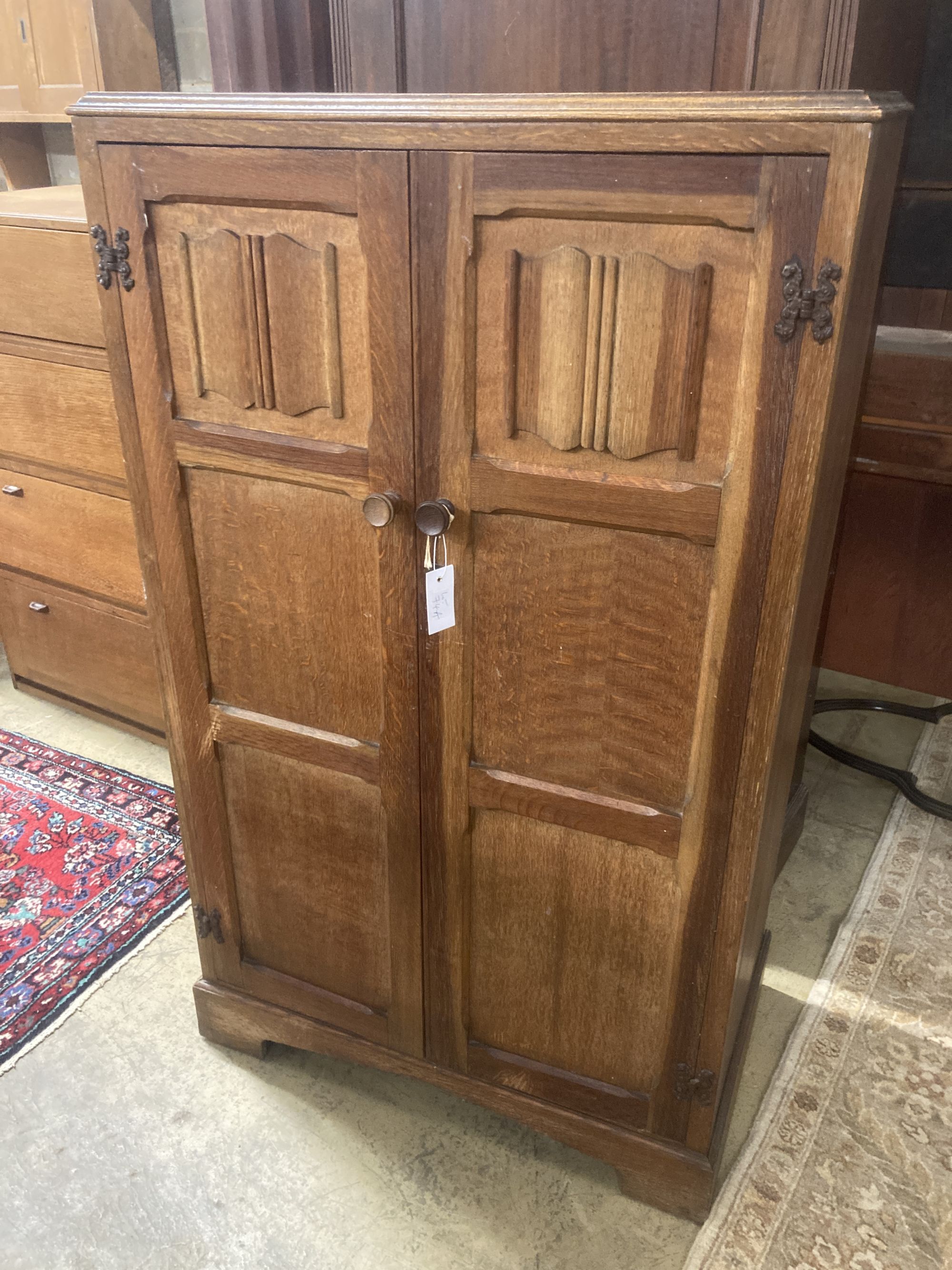 A light oak two door linen fold carved hanging cupboard, width 77cm, depth 46cm, height 131cm